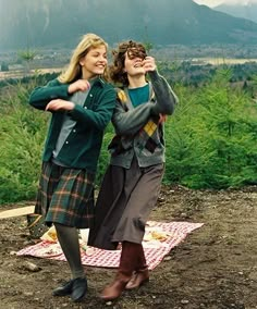 two women standing on top of a field with mountains in the background