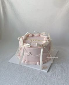 a pink cake with white ribbons on top