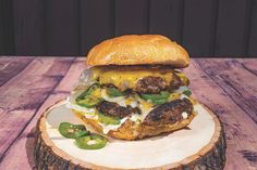 a hamburger sitting on top of a wooden table next to a slice of bread with cheese and green peppers