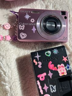 a pink camera sitting on top of a white blanket next to a cell phone case