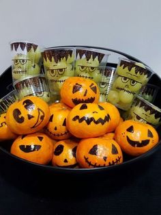 a bowl full of oranges with faces drawn on them and wrapped in plastic wrappers