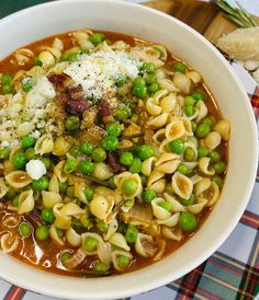 a bowl filled with pasta and peas on top of a checkered table cloth next to bread