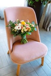 a pink chair with flowers on it sitting in front of a potted plant and window