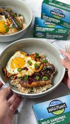 someone is holding a bowl of rice with an egg on top and some other food in the background