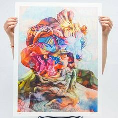 a person holding up a large painting with multiple colors on it's face and hands