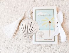 a card with a seashell on it next to a white ribbon and a tassel