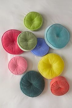 six different colored cushions arranged on a white surface, with one in the middle surrounded by smaller ones