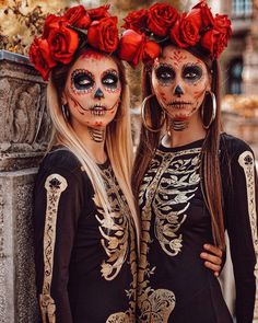 two women with skeleton makeup and red roses on their heads are standing next to each other