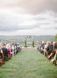 an outdoor ceremony with people sitting in chairs and facing the aisle to the side, on a cloudy day