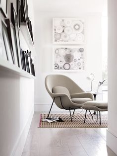 a chair and ottoman in a white room with pictures on the wall behind it,