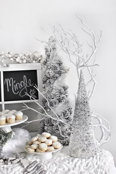 a table topped with cupcakes next to a chalkboard sign and trees covered in frosting