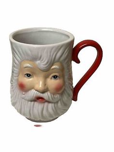 a ceramic mug with a santa claus face on it's side and red handles