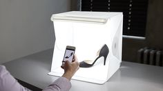 a woman holding a cell phone in front of a light box with high heels on it