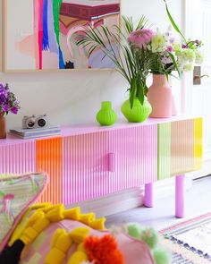 colorful vases and flowers sit on a pink dresser