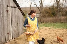 a woman in an apron is walking with chickens and eggs near a wooden barn on a farm