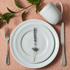 a white plate topped with a purple flower next to a cup and saucer on top of a pink table cloth