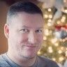 a man is smiling for the camera in front of a christmas tree with lights on it