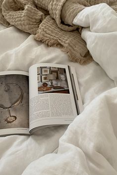 an open book sitting on top of a bed covered in white sheets and blankets next to a blanket