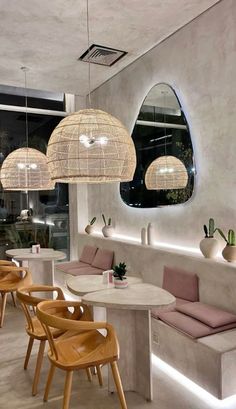 the interior of a restaurant with round tables and wooden chairs, hanging lights and circular mirrors