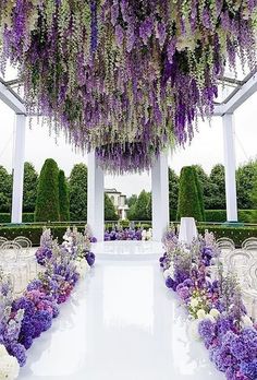 an outdoor wedding venue with purple and white flowers hanging from the ceiling over the aisle