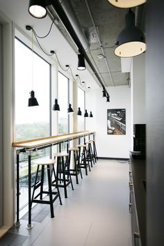 an empty bar with several stools and lights hanging from it's ceiling, in front of large windows