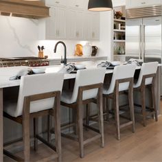 a large kitchen with white cabinets and counter tops, along with bar stools that match the hardwood flooring