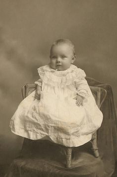 an old photo of a baby sitting in a chair