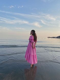 a woman in a pink dress standing on the beach