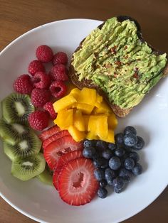 a white plate topped with toast, fruit and avocado on top of a wooden table