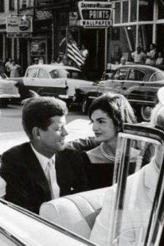 an old black and white photo of two people in a car talking to each other