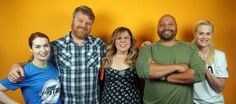 a group of people standing next to each other in front of a yellow wall with their arms crossed