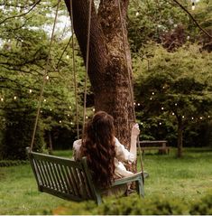 a woman sitting on a green bench next to a tree and string lights hanging from the branches