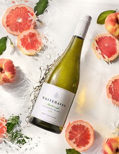 a bottle of white wine surrounded by grapefruits