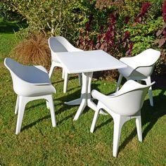 a white table and chairs sitting on top of a grass covered field next to bushes