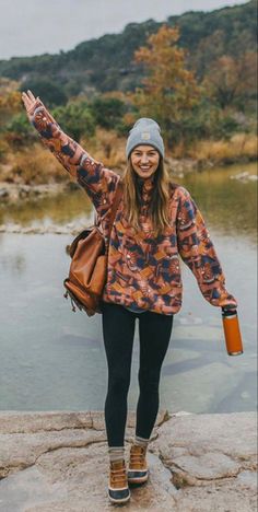 a woman standing on top of a rock next to a body of water with her arms in the air