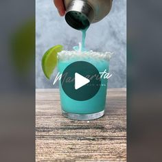 a person is pouring something into a blue drink with a lime slice on the rim