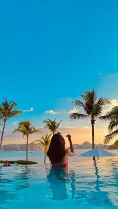 a woman standing in the middle of a pool with palm trees around her and an ocean view behind her