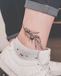 a woman's foot with a tattoo on the ankle and an olive branch behind her