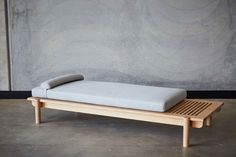 a wooden bench with a cushion on it in front of a concrete wall and floor