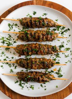 several skewers of meat with herbs on them sitting on a white platter