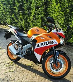 an orange and white motorcycle parked in front of a hedge on a cobblestone road