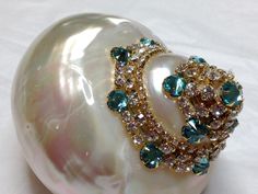 a pearl and diamond ring sitting on top of a white shell with blue stones in the middle