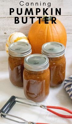 three jars filled with pumpkin butter sitting on top of a table next to a whisk