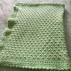 a green crocheted blanket laying on top of a bed