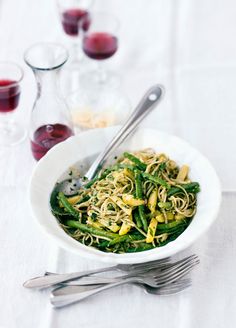 a white bowl filled with green beans and noodles next to two glasses of red wine