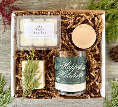 an open gift box containing a candle, soap and some other holiday items on a table