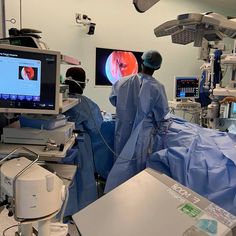 an operating room with medical equipment and monitors on the wall, two doctors in blue gowns