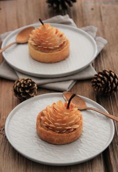 two white plates topped with desserts on top of wooden table next to pine cones