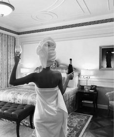 a woman in a bathrobe holding a wine glass and looking at the bed