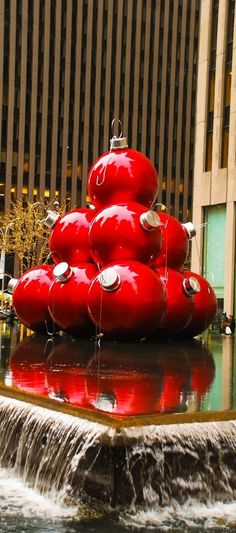 a christmas tree made out of red balls in the middle of a fountain with water running down it